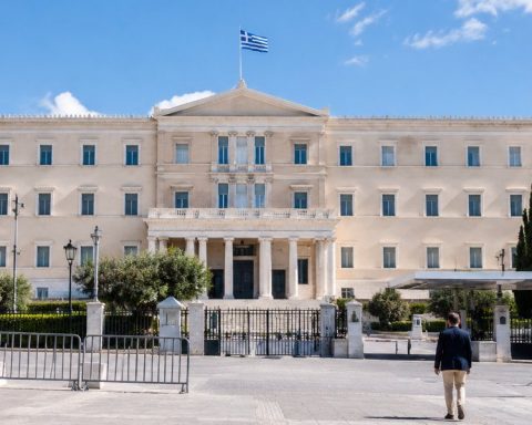 Πρόσοψη υπουργείου στην Ελλάδα, με πεζοδρόμιο, ασπίδες ασφαλείας και μακρινούς περαστικούς από πίσω.